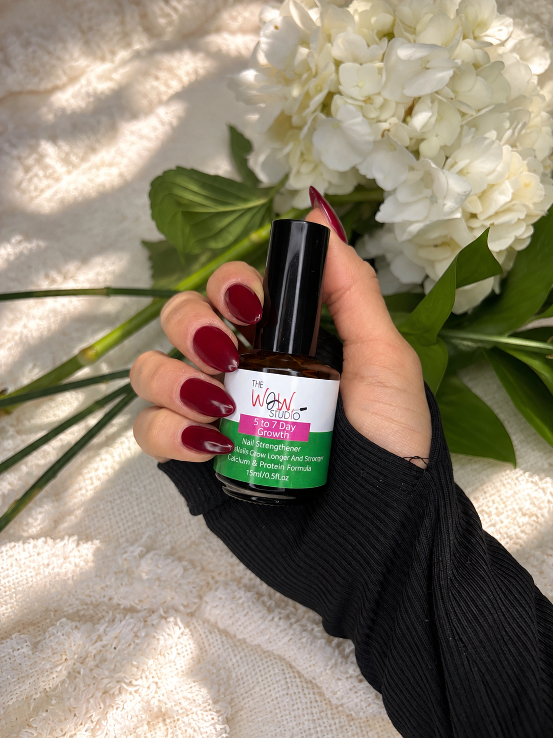 The WOW Studio Nail Strengthener held in hand with white flowers